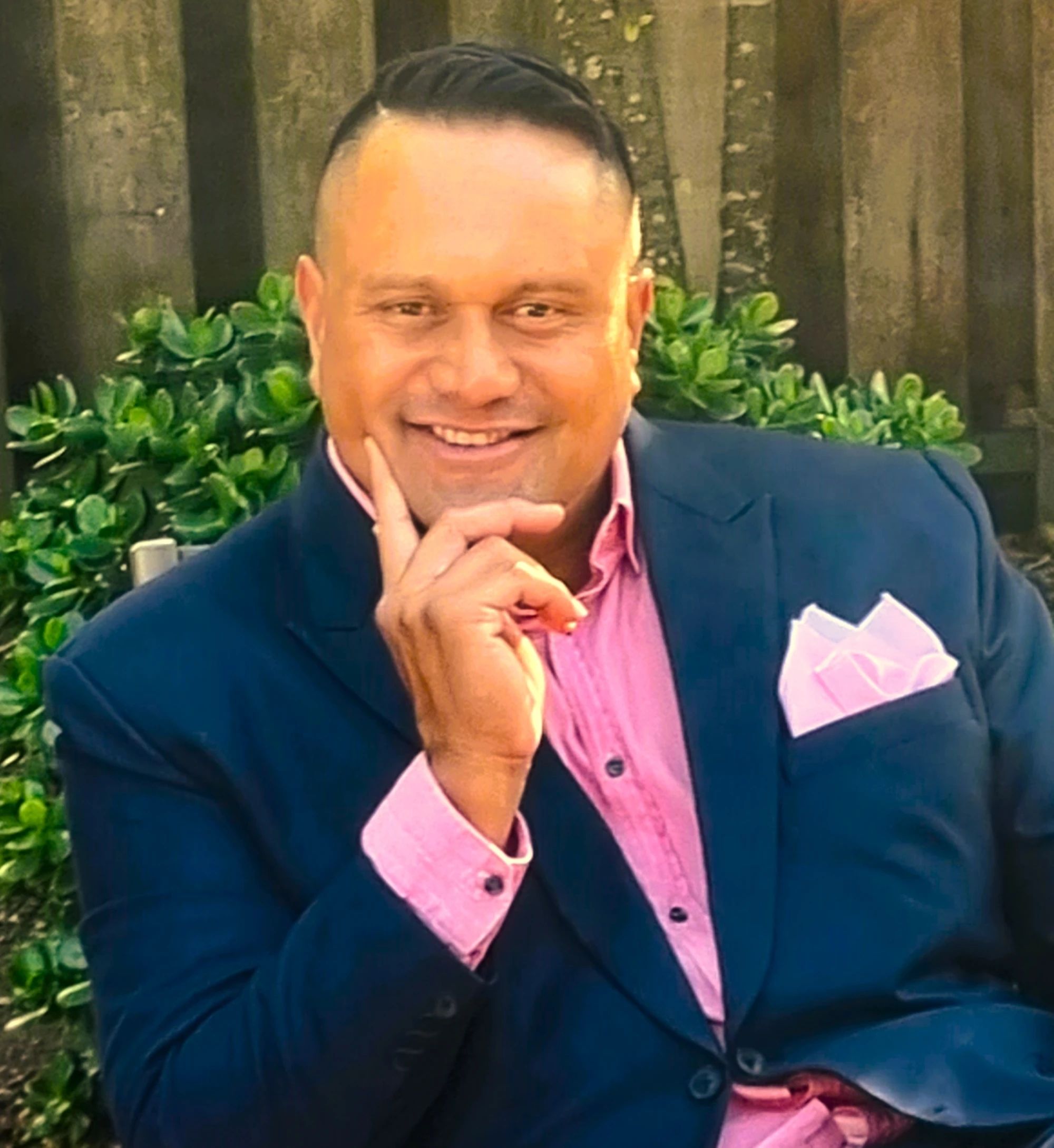Gabe Tuhoro, founder of Epoch, smiling in a navy jacket and pink shirt in front of a garden fence