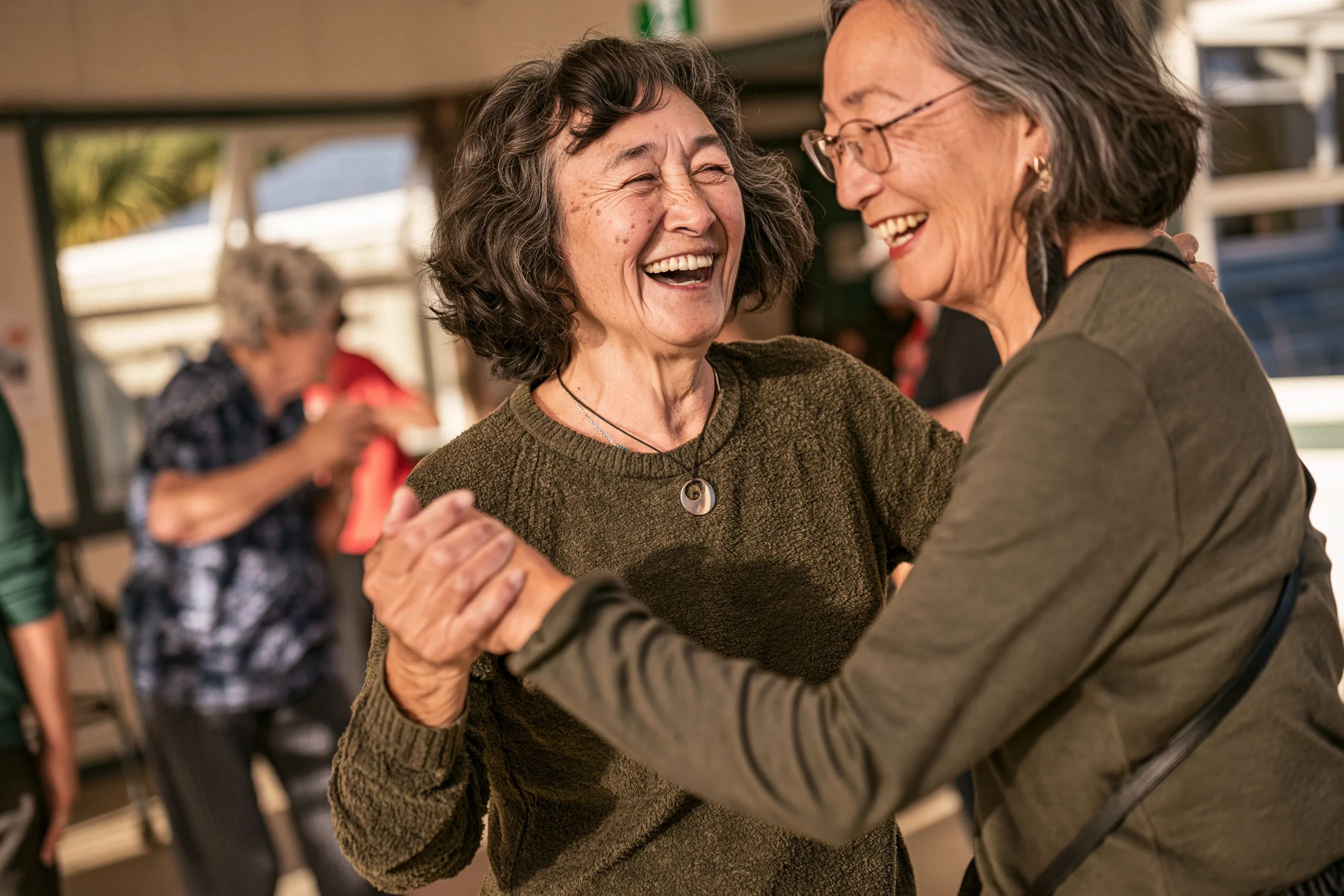 Two older women laughing as they dance together, hands clasped